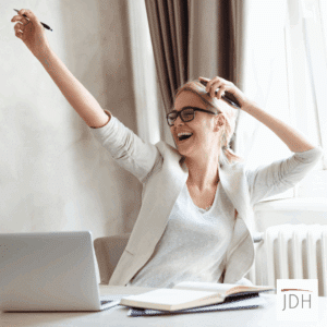 Woman sitting in front of a laptop, smiling with arms in the air